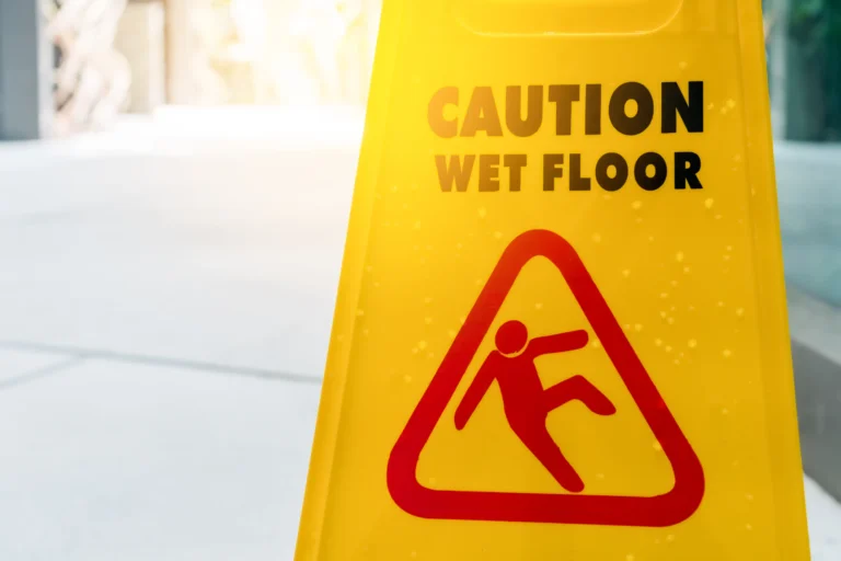 Yellow caution sign with CAUTION WET FLOOR in black text and a red slip hazard symbol, often used in Premises Liability Defense cases.