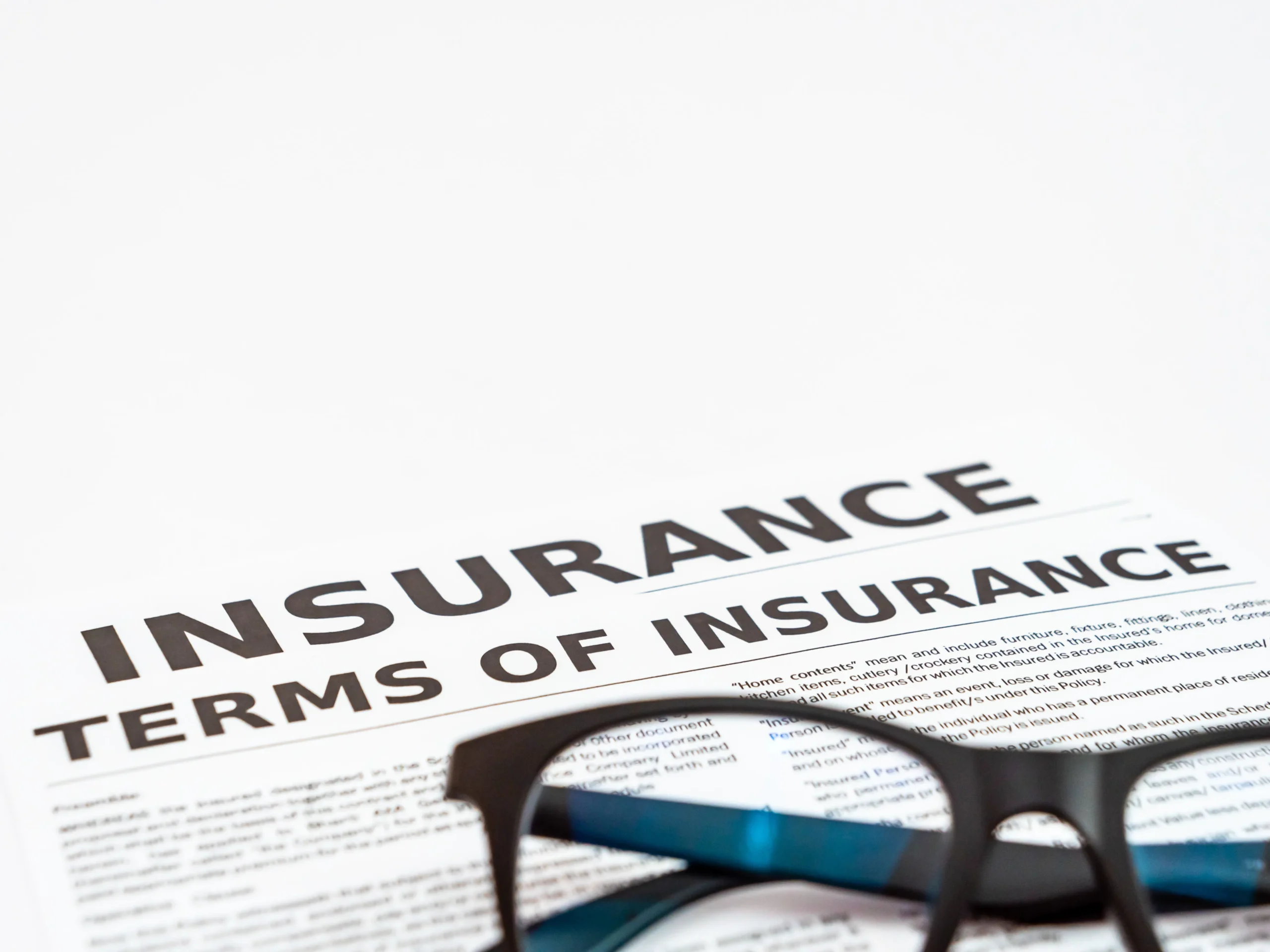 A close-up of a document titled Insurance Terms of Insurance with eyeglasses resting on top, capturing the concept of reading insurance policies.