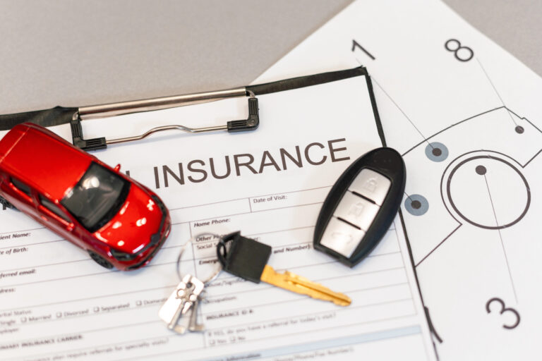 A car insurance form on a clipboard, a red toy car, car keys, and a document with a diagram are arranged on a table.