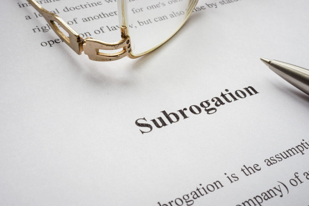 A sheet of paper with the word Subrogation in bold text, alongside a pair of eyeglasses and the tip of a pen.