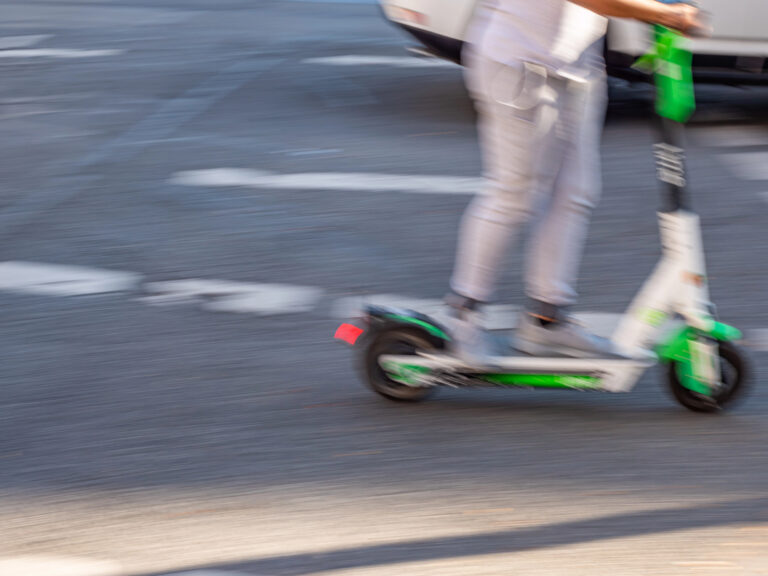 A person riding an electric scooter on a city street, image blurred to show motion.