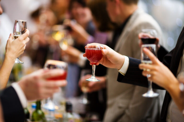 People in formal attire clink glasses filled with red beverages at a social gathering or celebration.