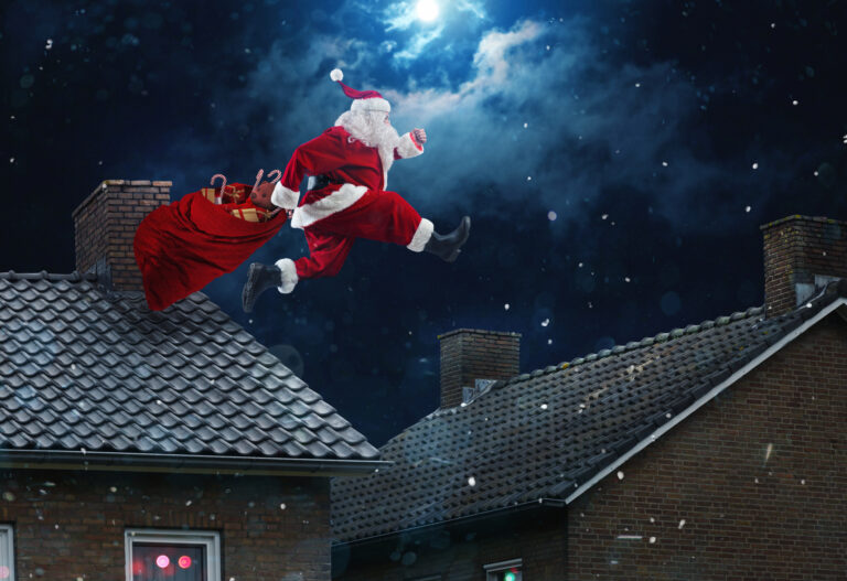 Santa Claus jumps between rooftops at night, carrying a red sack of gifts under a cloudy, moonlit sky.